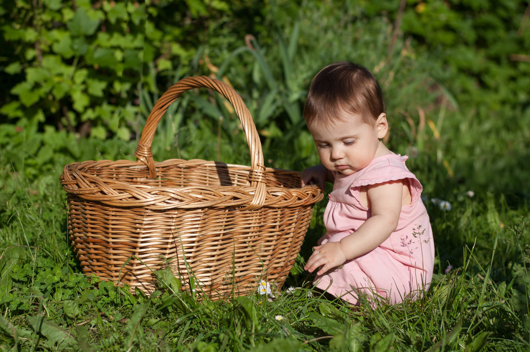 Très jeune enfant dans l'herbe à côté d'un panier en osier